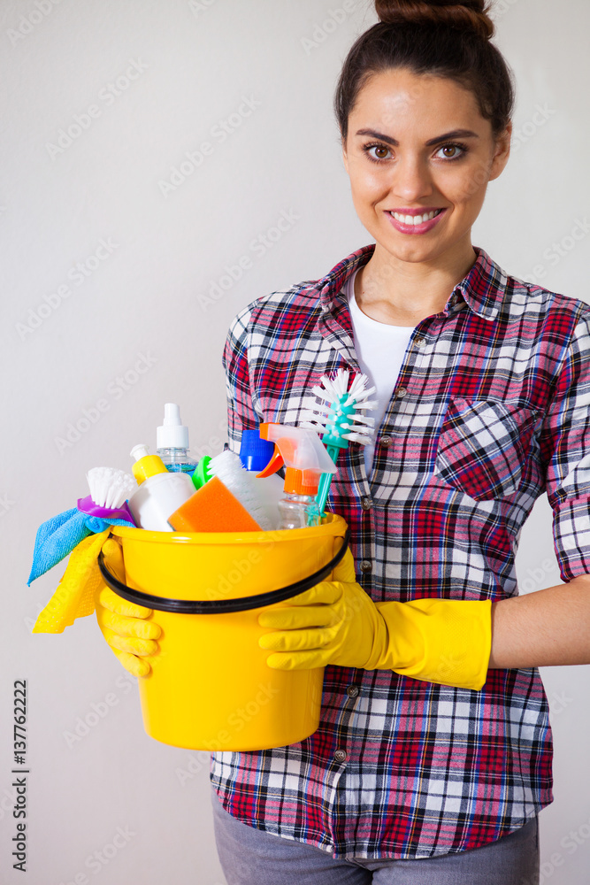Young pretty woman holding cleaning tools and products in bucket, on white citchen, cleaning concept Young pretty woman holding cleaning tools and products in bucket, on white citchen, cleaning concept