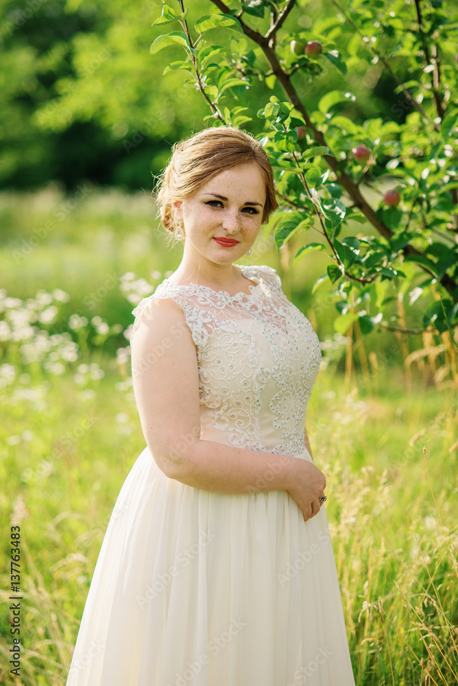 Young overweight girl at beige dress posed background spring garden. Young overweight girl at beige dress posed background spring garden.