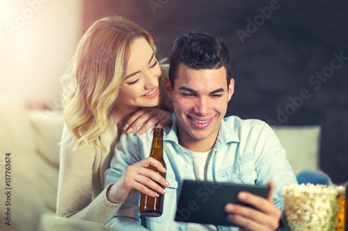 Young couple sitting on the couch in a living room and looking at digital tablet