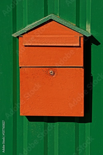 Красный почтовый ящик на железном зелёном заборе