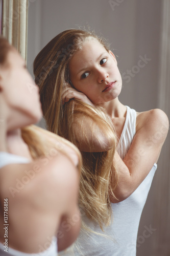 Teenage girl checking her face and hairs in the mirror