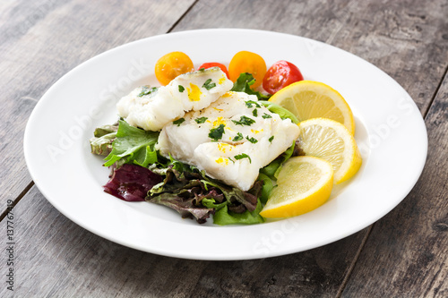 Fried cod fillet and salad in plate on wooden background

