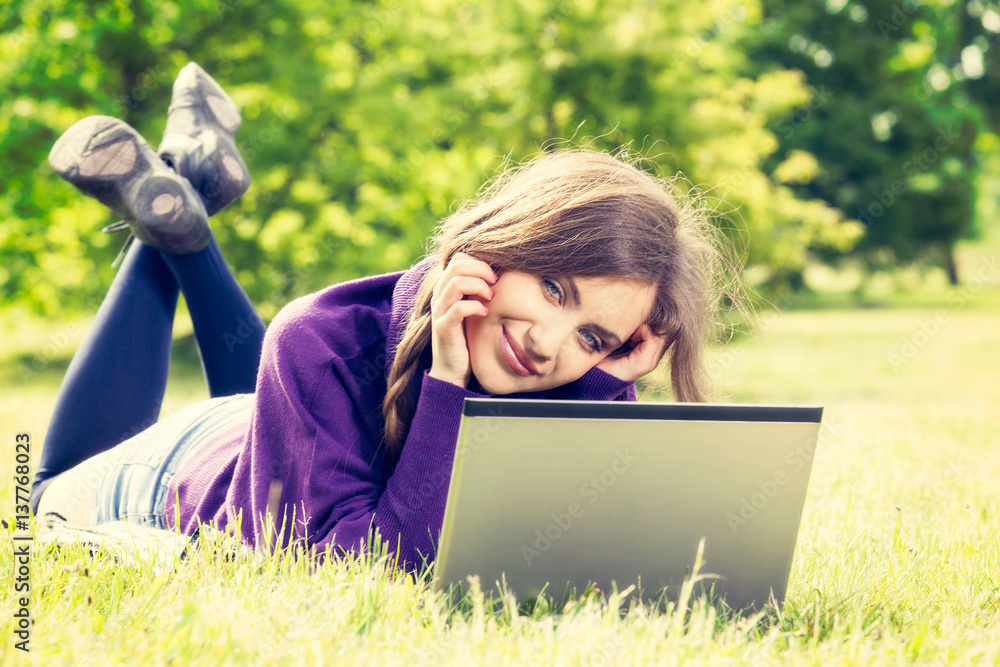 Young woman using laptop in the park lying on the green grass Young woman using laptop in the park lying on the green grass