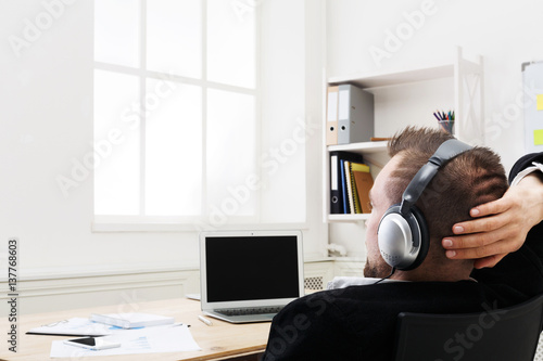 Over shoulder shot of businessman in office listen music in headphones
