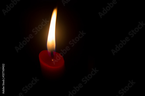 Red candle with yellow flame on black background