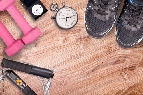 Fitness gym and running equipment. Stopwatch and running shoes, jumping rope and music player. Time for fitness. Sport running accessories on the wooden floor.
