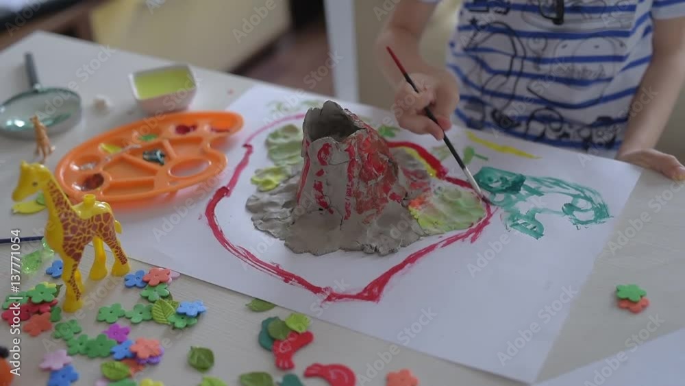 Boy painting clay in the shape of a volcano .Young little boy painting on the paper Boy painting clay in the shape of a volcano .Young little boy painting on the paper