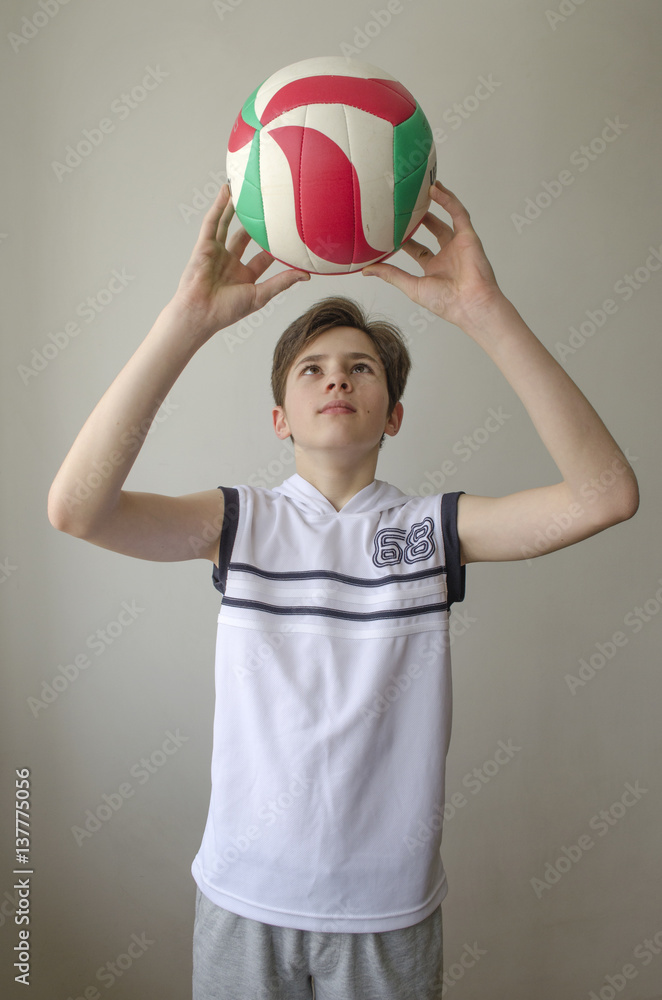 Teenager boy in a white shirt with a ball for volleyball on a light background
