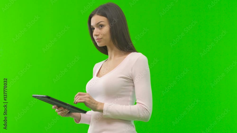 The woman with a tablet stand on the green screen background The woman with a tablet stand on the green screen background