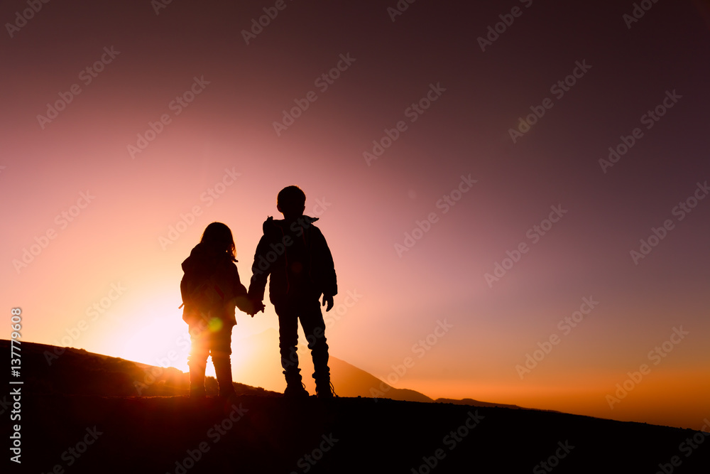 Silhouettes of little boy and girl hiking at sunset