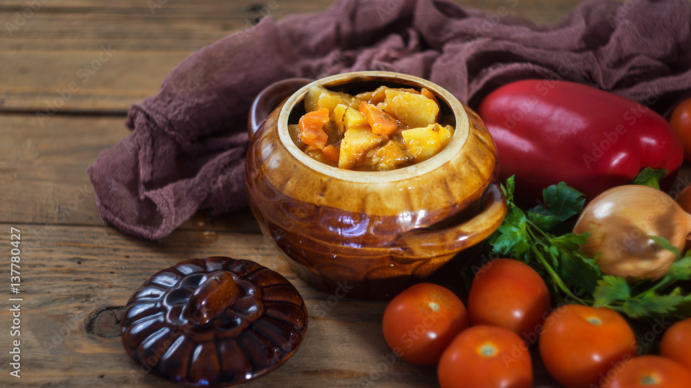 Vegetable Stew in Brown Pot with Raw Vegetables on Wooden background