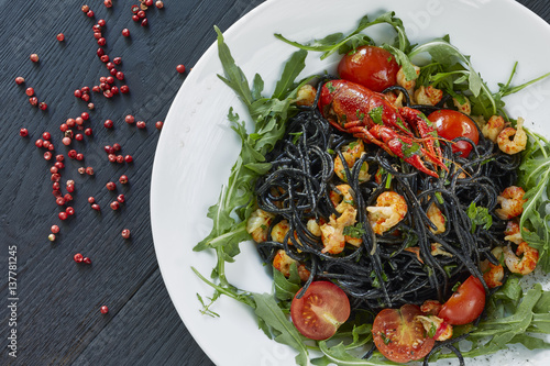 Black spaghetti with crayfish, fresh green arugula, cilantro, pepper and olive oil on a dark wooden table. 