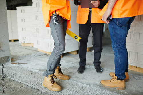 Low section shot of legs of two construction workers wearing jeans and brown leather work boots standing with man in suit on concrete floor