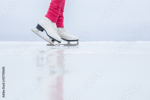 Woman skating with white skates on the ice area at the seashore in winter day. Weekends activities outdoor in cold weather.