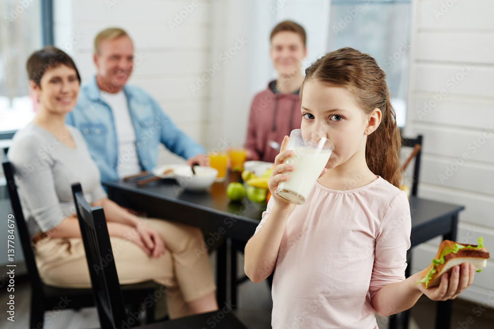 Little girl drinking milk from glass and eating vegetable sandwich Little girl drinking milk from glass and eating vegetable sandwich