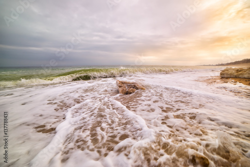 beautiful view of the sea spring. Chunks of ice in the sand  a wave with foam incident on the beach  a gentle soft sunlight. A beautiful evening on the sea.  