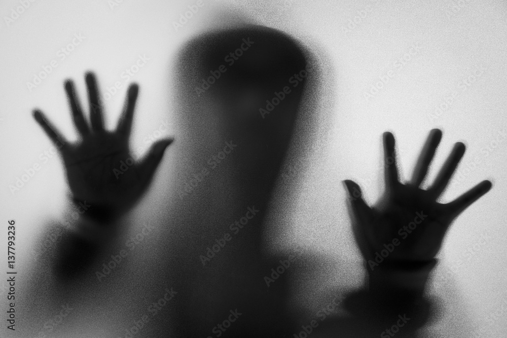 Shadow blur of horror man in jacket with hood.Hands on the glass.Dangerous man behind the frosted glass.Mystery man.Halloween background.Black and white picture.Blur picture.