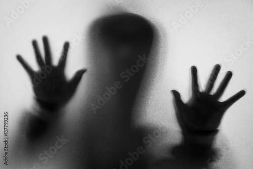 Shadow blur of horror man in jacket with hood.Hands on the glass.Dangerous man behind the frosted glass.Mystery man.Halloween background.Black and white picture.Blur picture.