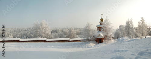 Snow covered orthodox chapel with brick fence on the background of hoary forest