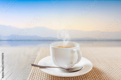 hot coffee in white cup on vintage wooden table and calmnesss lake background