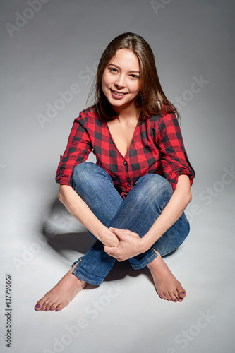 Billede på lærred Smiling teen girl wearing jeans and red checked shirt with teeth brackets sittin