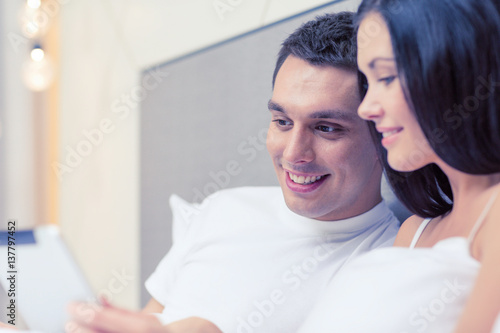 smiling couple in bed with tablet pc computers