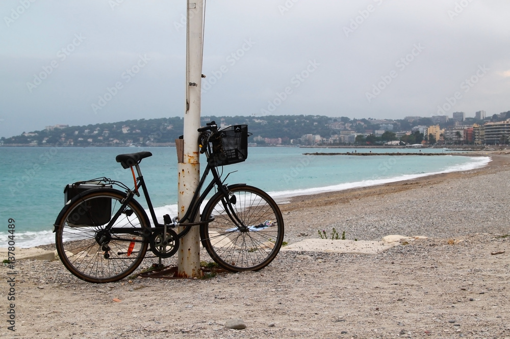 Obraz premium Lonely bicycle on beach on cloudy rainy day. Beach in Menton, town in South of France.