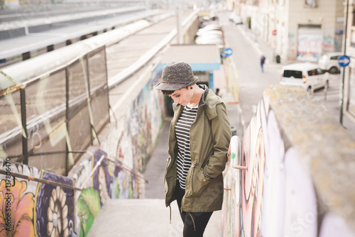 Young beautiful caucasian short hair woman looking down outdoor in the city, smiling - shy, timid, demure concept