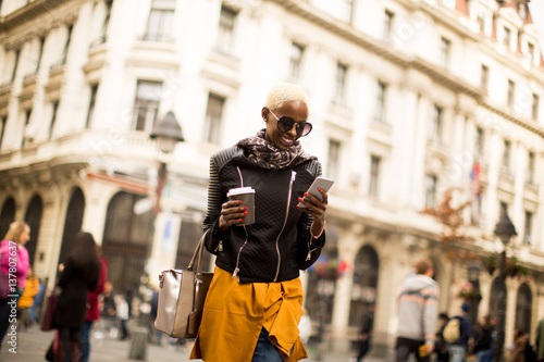 Beautiful stylish african american woman holding coffee and using a smart phone