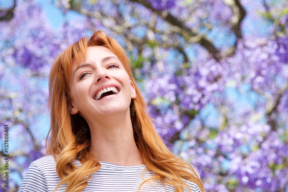 Naklejka premium attractive young woman laughing by tree with purple flowers