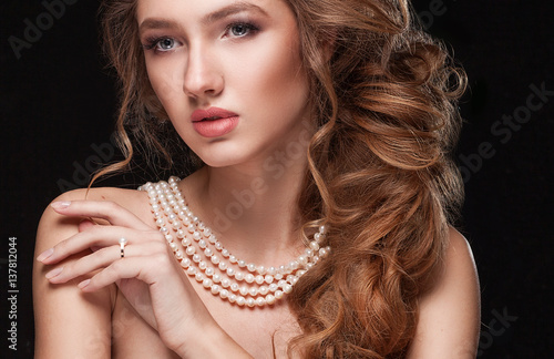 Beautiful elegant woman in pearl necklace, long curly tress over black background. Fashion glamour portrait.