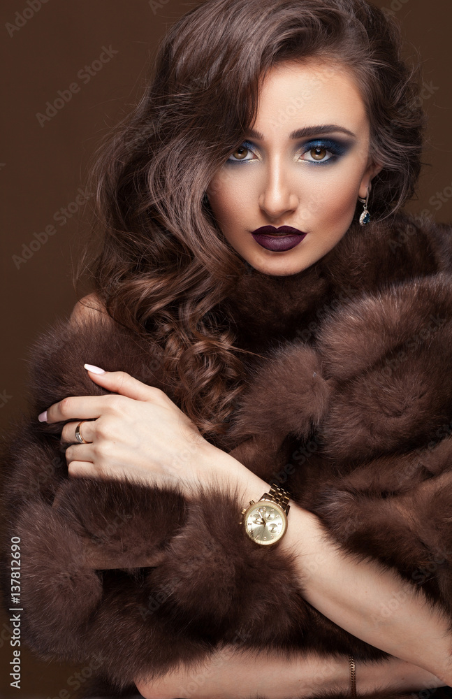 Luxury elegant woman in fur coat, golden earrings and watches. Glamour beautiful look. Rich lady over dark chocolat background. Luxury elegant woman in fur coat, golden earrings and watches. Glamour beautiful look. Rich lady over dark chocolat background.