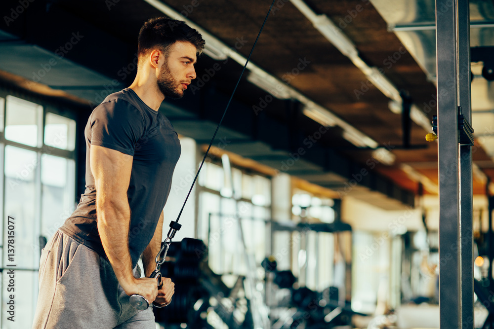 Naklejka premium Handsome man doing heavy weight exercise for triceps in the gym