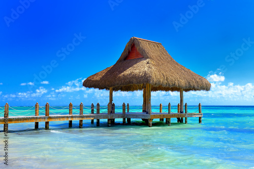 Tropical white sandy beach. Palm leaf roofed wooden pier with gazebo on the beach. Punta Cana  Dominican Republic