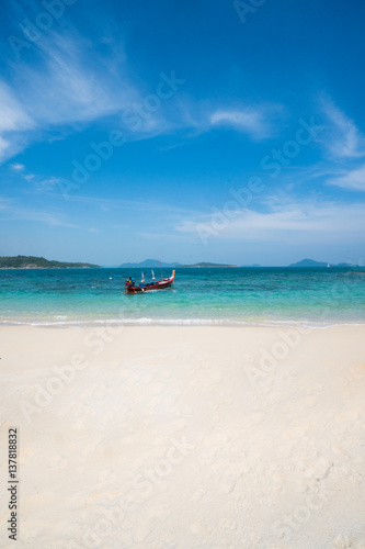 Beautiful vertical view from sandy beach on longtail boat tied on turquoise sea shore in sunny summer day isolated over blue sky background