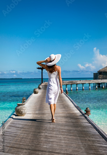 Modische Frau mit weißem Hut läuft auf einem Steg auf den Malediven