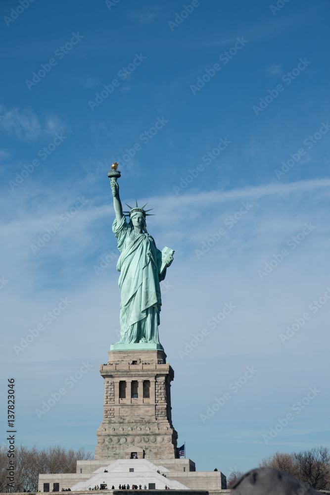 Obraz premium Lady Liberty on her pedestal. Statue of Liberty overlooking New York Harbor on a sunny day with blue skies and wispy clouds. Liberty Island, New York City, USA.