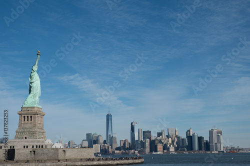 Statue of Liberty in Profile with Manhattan skyline in background. Bright sunny day  Wall Street and Financial District of lower Manhattan in the background.  View from ferry across the harbor.