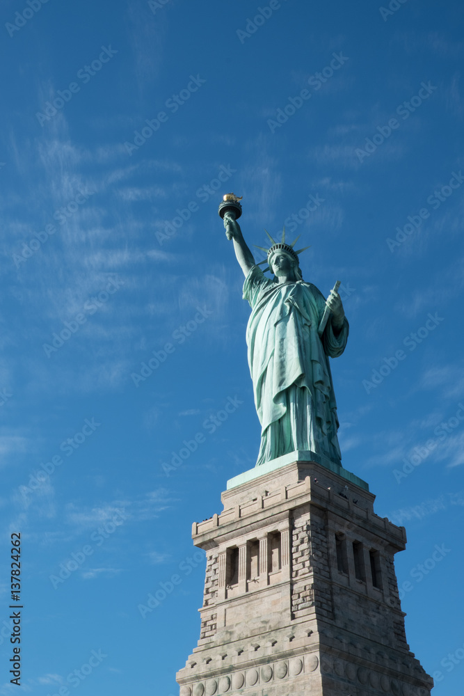 Lady Liberty by Bartholdi based on the Colossus of Rhodes, isolated with no buildings in the background.  Statue of Liberty on her pedestal with beautiful blue skies and a few wispy clouds.