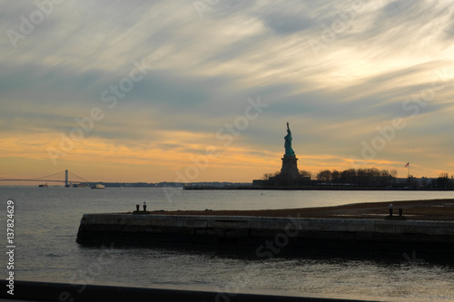 Statue of Liberty at sunset with dramatic clouds.  Silhouette of the Statue of Liberty at dusk, view of the Statue of Liberty from local ferry. Liberty Island at sunset.