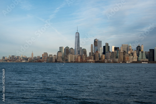 Famous New York City skyline and New York Harbor as seen from a boat.  Blue skies and cirrus clouds over New York s Financial district.  Sunny day looking at Manhattan from the water.