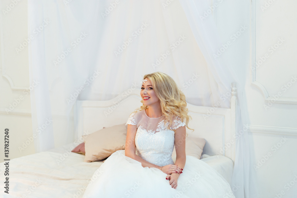 Beautiful bride woman sitting on bed in white bedroom, smiling happy Beautiful bride woman sitting on bed in white bedroom, smiling happy