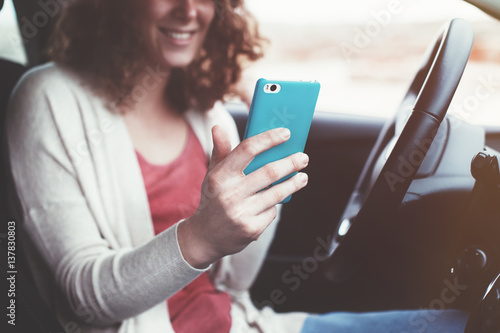 Happy curly woman sitting in non moving car and using mobile phone