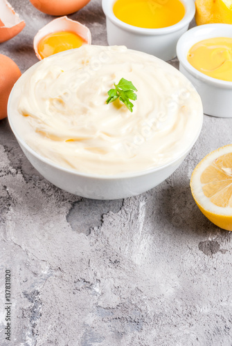 Mayonnaise with ingredients for cooking - eggs, vegetable oil, mustard, lemon, parsley. On the grey stone concrete table close view copy space