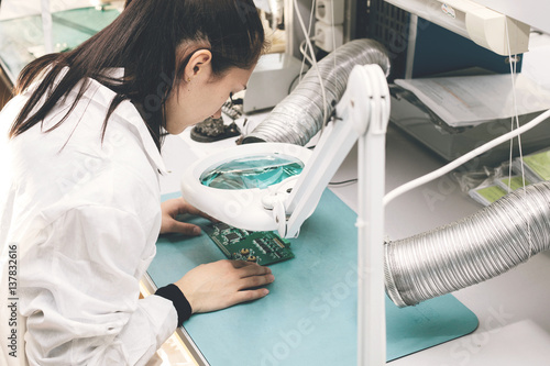 Beautiful female computer expert professional technician examining board computer in a laboratory in a factory. Troubleshooting. Technical support. Engineering. Manufacturing.