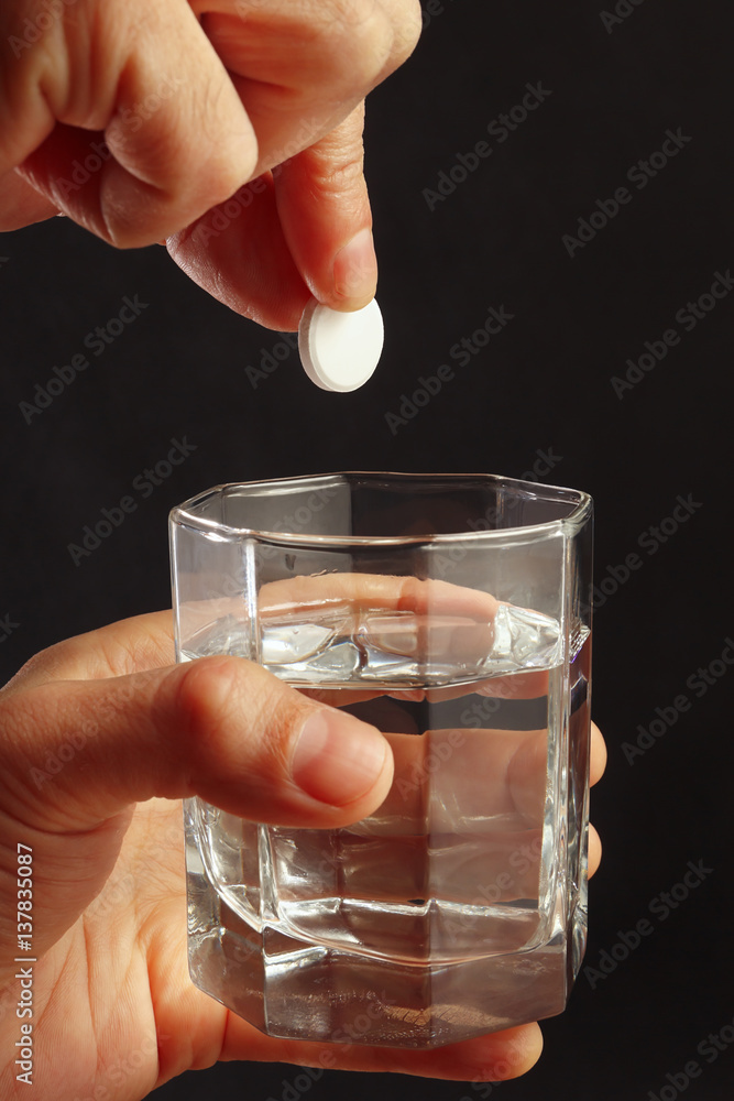 Hand throwing an effervescent tablet from headache in a glass of water on a dark background. Hand throwing an effervescent tablet from headache in a glass of water on a dark background.