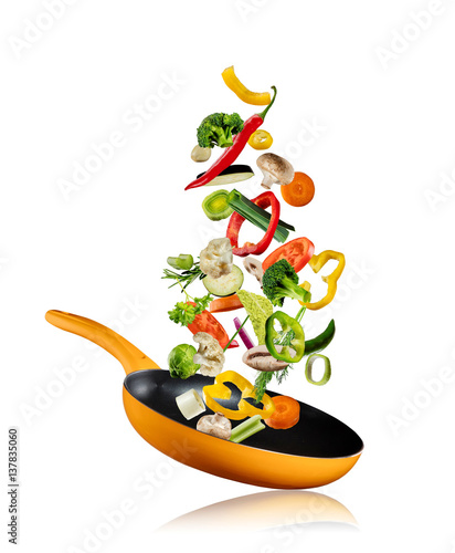 Fresh vegetables flying into a pan on white background