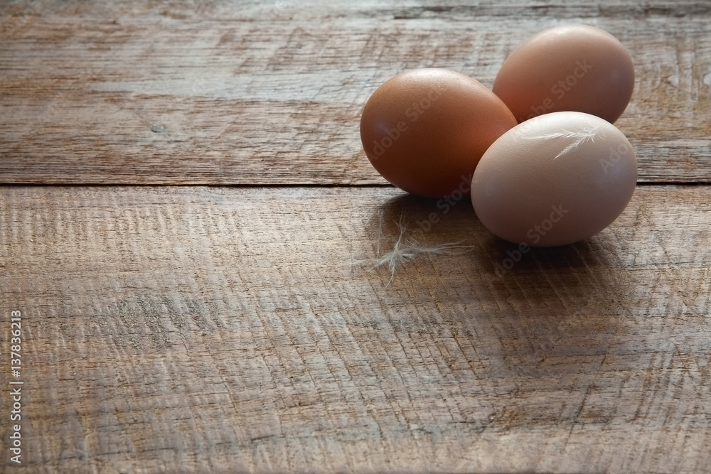 Three Fresh Farm Chicken Eggs with Feathers on Rustic Dark Brown Wooden Table Horizontal with Copy Space Three Fresh Farm Chicken Eggs with Feathers on Rustic Dark Brown Wooden Table Horizontal with Copy Space