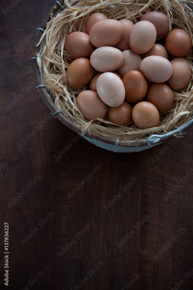 Vertical Top View of Fresh Farm Chicken Eggs in Metal Wire Basket with Raffia on a Dark Brown Wooden Table Vertical Top View of Fresh Farm Chicken Eggs in Metal Wire Basket with Raffia on a Dark Brown Wooden Table