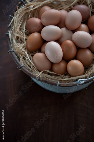 Vertical Close Up Top View of Fresh Farm Chicken Eggs in Metal Wire Basket with Raffia on a Dark Brown Wooden Table